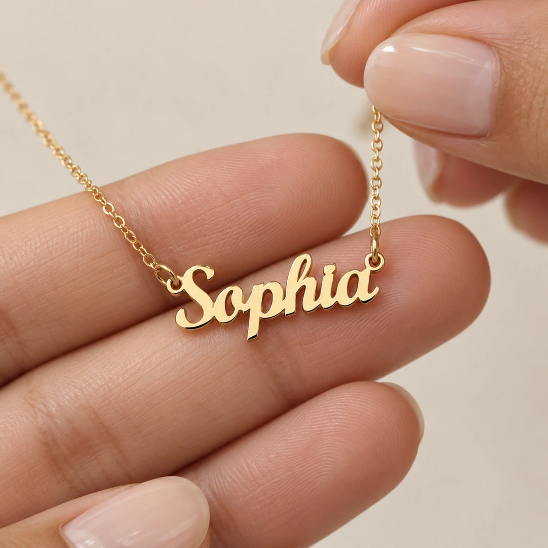 Hand holding the gold Name necklace between thumb and fingers