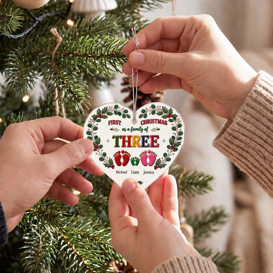 Hands holding the First Christmas family heart ornament with footprints in front of the Christmas tree