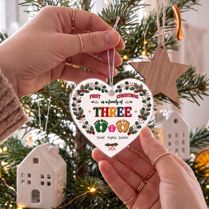 Hands holding the family footprint ornament for a family of three at the Christmas tree