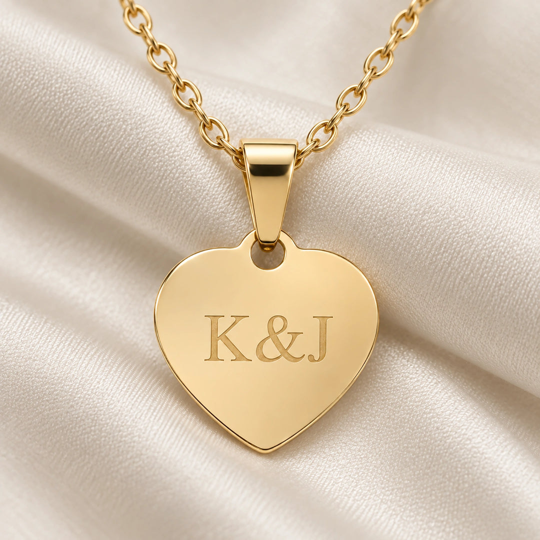 Gold heart pendant of the Love necklace engraved with initials on a silky fabric