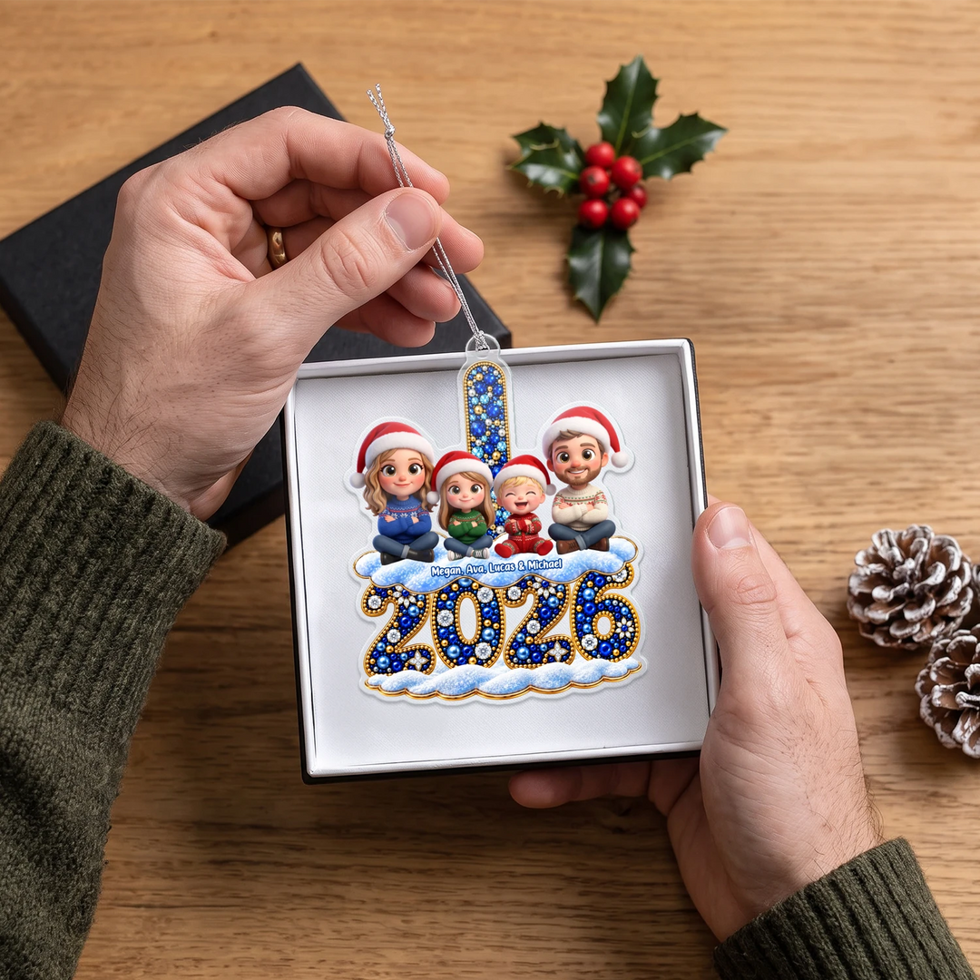 Hands holding the personalized 2026 family ornament with figures in Santa hats in a white gift box
