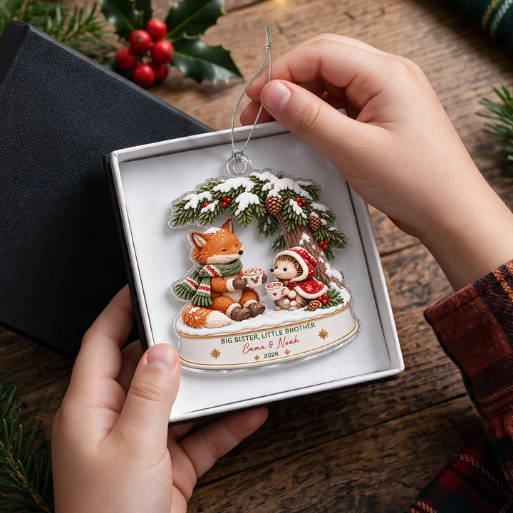 Hands lift the Fox and Hedgehog sibling ornament out of a gift box