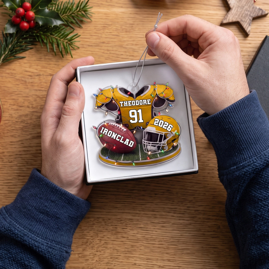Hands lift the yellow Football ornament out of a gift box
