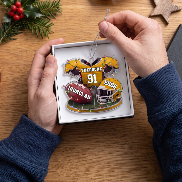 Hands lift the yellow Football ornament out of a gift box