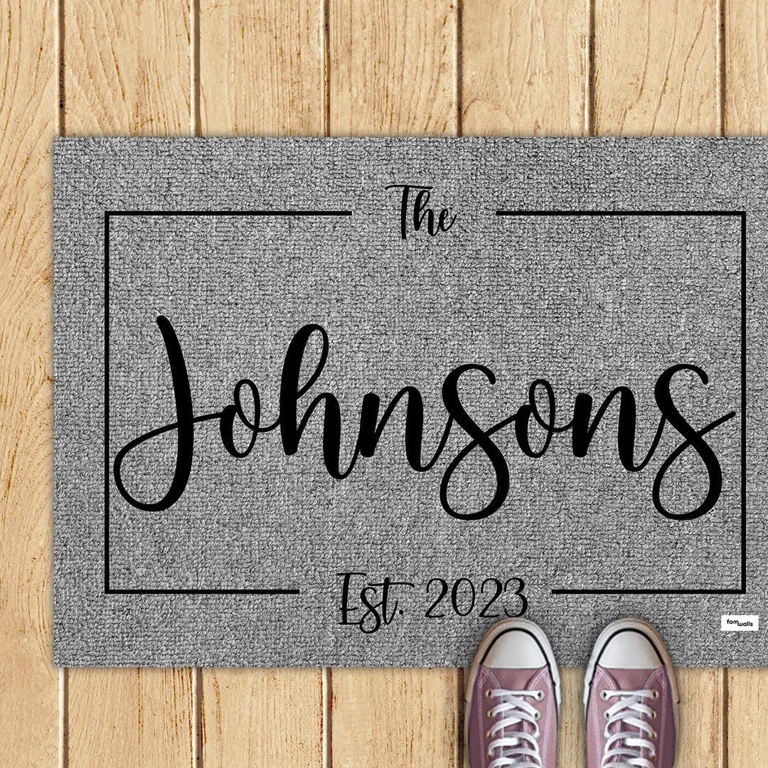 Gray family name doormat with pink sneakers on a wooden deck