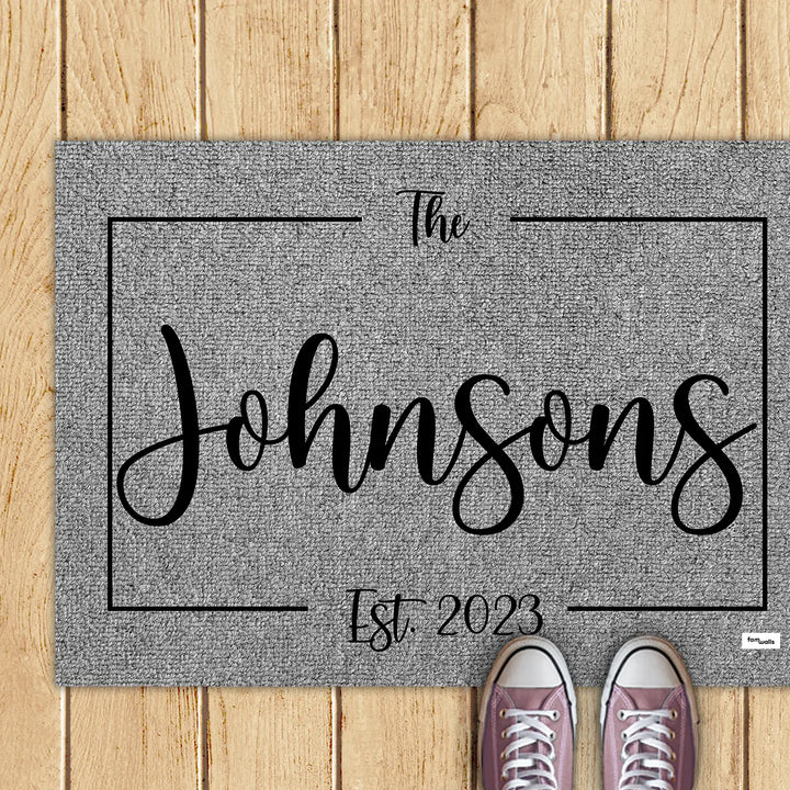 Gray family name doormat with pink sneakers on a wooden deck