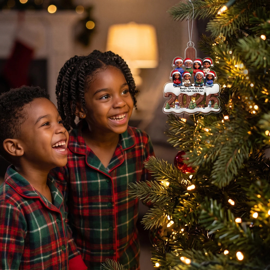 Two smiling kids in plaid pajamas looking at their family ornament on a lit Christmas tree