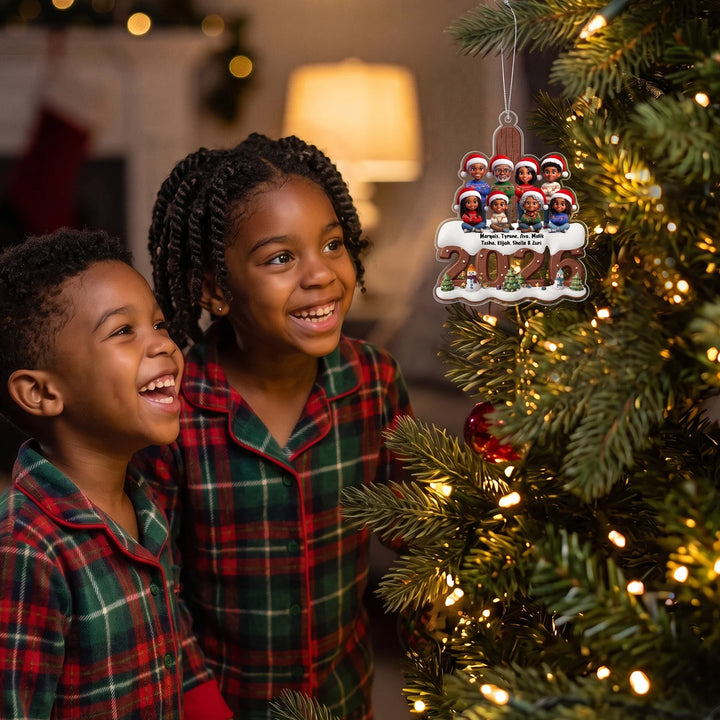 Two smiling kids in plaid pajamas looking at their family ornament on a lit Christmas tree